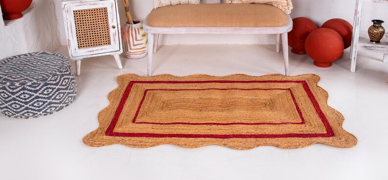 May include: A rectangular jute rug with a red border and a wavy edge. The rug has a natural, earthy tone and is perfect for adding a touch of warmth and texture to any room.