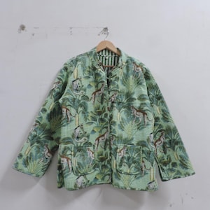 Puede incluir: Chaqueta acolchada verde claro con estampado de jungla con monos y follaje. La chaqueta tiene mangas largas, dos bolsillos delanteros y un forro a rayas. Cuelga de una percha de madera.