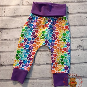 May include: Purple baby leggings with a rainbow heart print. The leggings have a wide waistband and cuffed ankles.