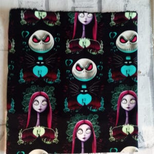 Può includere: Tessuto nero con un motivo ripetuto di Jack Skellington e Sally da The Nightmare Before Christmas. Il design include il volto di Jack, il volto di Sally e altri elementi tematici in verde acqua, rosso e bianco.