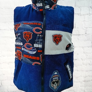 May include: A blue Chicago Bears vest with a full-length zipper. The vest features various patches and patterns, including the team's logo, stadium imagery, and the word "BEARS." The vest is displayed on a mannequin.