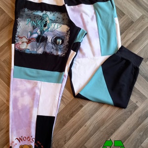 Può includere: Pantaloni da jogging in patchwork nero, bianco e turchese con una stampa grafica di Pink Floyd "The Wall" sulla gamba sinistra. I pantaloni da jogging hanno una cintura con coulisse e polsini elastici. La parte inferiore della gamba sinistra ha una toppa nera con il testo "Woo's Fashion" in rosso.
