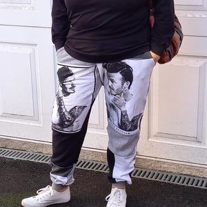 Può includere: Pantaloni della tuta neri e bianchi con un design a patchwork che presenta un'immagine ripetuta di David Beckham. I pantaloni della tuta hanno una cintura con coulisse e caviglie a polsino.