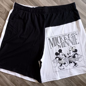 Puede incluir: Pantalones cortos de dormir negros y blancos con un panel blanco que presenta a Mickey Mouse y Minnie Mouse con el texto "Mickey and Minnie".