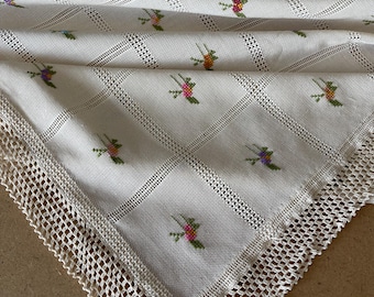 Könnte beinhalten: Eine weiße Häkeltischdecke mit einem zarten Blumenmuster und einer Spitzenbordüre. Die Tischdecke ist aus einem feinen, leichten Stoff gefertigt und hat einen dezenten Glanz.