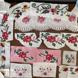 May include: Assortment of embroidered fabric pieces featuring floral designs. The pieces include white and pink backgrounds with red, yellow, and purple flowers. Some pieces have a scalloped edge.