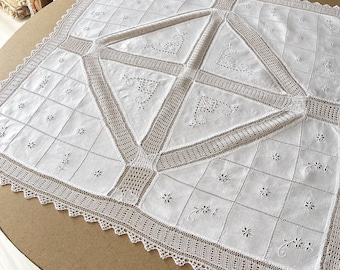 Könnte beinhalten: Weiße Häkeltischdecke mit einem zarten Blumenmuster und einem geometrischen Design. Die Tischdecke hat einen gewellten Rand und ist aus feinem Leinen gefertigt.