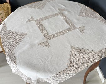 Könnte beinhalten: Eine weiße Tischdecke aus Leinen mit zarter Häkelspitze und aufwendigen Stickereien. Die Tischdecke hat ein zentrales quadratisches Design mit vier kleineren Quadraten an jeder Ecke.