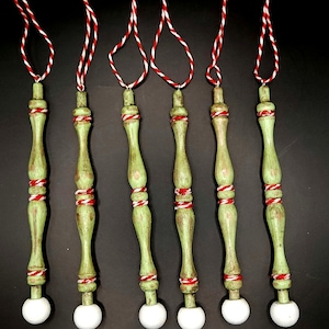 May include: Six green wooden ornaments with white tops and red and white twine. The ornaments are tied with a red and white twine loop.