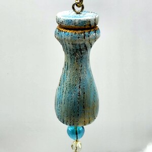 May include: A blue and gold wooden ornament with a gold chain and blue and clear glass beads. The ornament is painted in a distressed style, giving it a vintage look.