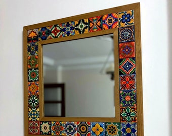 May include: A square mirror with a wooden frame decorated with colourful, patterned tiles. The tiles are arranged in a border around the mirror, creating a vibrant and eye-catching design.