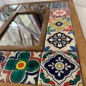 May include: A wooden framed mirror with a colourful mosaic tile border. The tiles feature a variety of floral and geometric patterns in shades of blue, green, yellow, red and white.