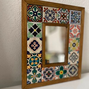 May include: A wooden framed mirror with a colourful mosaic tile design. The tiles are in various shades of blue, green, red, yellow, and white. The mirror is rectangular and has a simple, clean design.