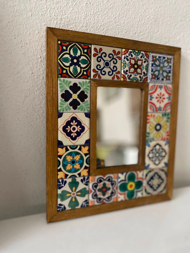 May include: A wooden framed mirror with a colourful mosaic tile design. The tiles are in various shades of blue, green, red, yellow, and white. The mirror is rectangular and has a simple, clean design.
