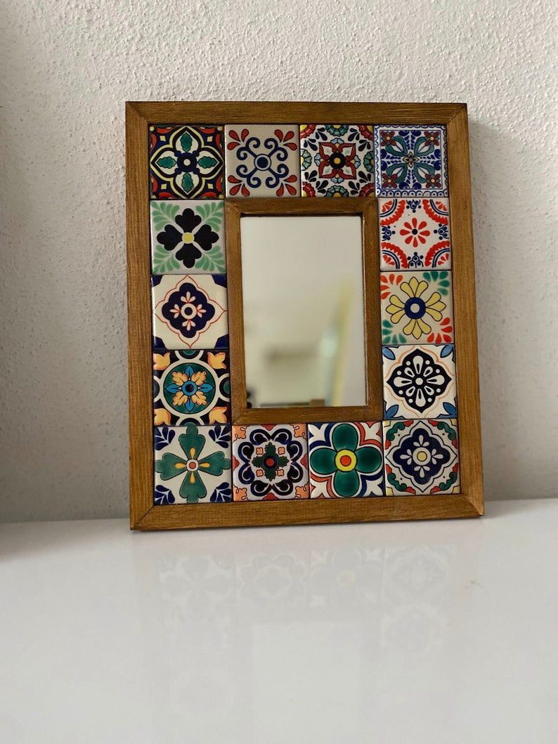 May include: A wooden framed mirror with a colourful mosaic of tiles surrounding the reflective surface. The tiles feature a variety of floral patterns in shades of blue, green, yellow, red, and white.