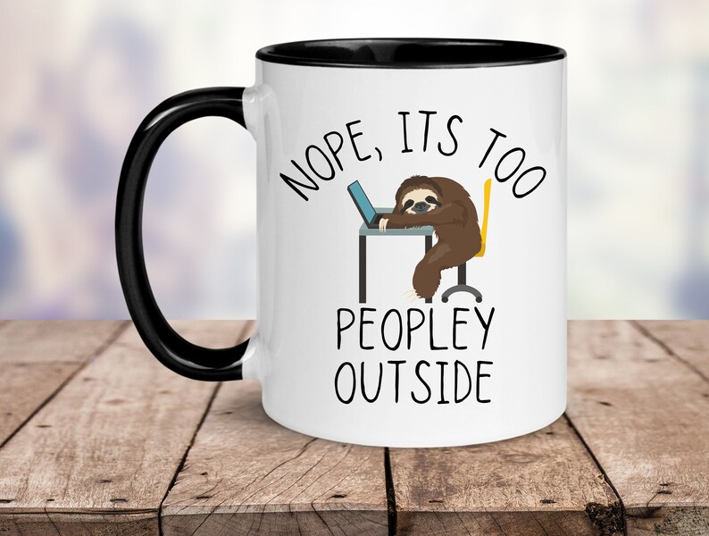 May include: White ceramic mug with a black rim and handle. The mug features a cartoon sloth sitting at a desk with a laptop, and the text "NOPE, IT'S TOO PEOPLEY OUTSIDE".