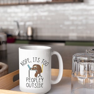May include: White ceramic mug with a black and brown sloth illustration. The mug has the text "NOPE, ITS TOO PEOPLEY OUTSIDE" printed on it.