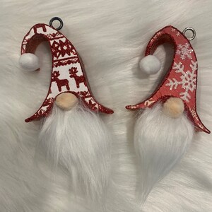 May include: Two red and white Christmas gnomes with white fur beards. One gnome has a snowflake pattern on its hat and the other has a reindeer pattern.
