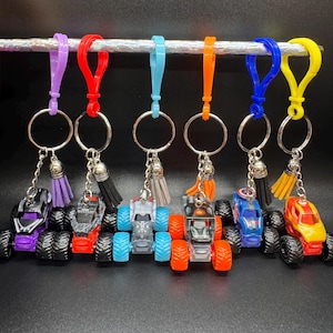 Puede incluir: Una colecci&oacute;n de llaveros de monster trucks coloridos. Cada llavero presenta un mini monster truck con neum&aacute;ticos negros grandes, una borla y un llavero de metal. Los llaveros son de varios colores, incluyendo morado, rojo, azul, naranja y amarillo.
