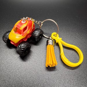 Puede incluir: Un llavero de cami&oacute;n monstruo amarillo y rojo con neum&aacute;ticos negros. El llavero incluye un llavero plateado, un cierre amarillo y una borla amarilla. El cami&oacute;n tiene un dise&ntilde;o detallado y est&aacute; hecho de pl&aacute;stico.