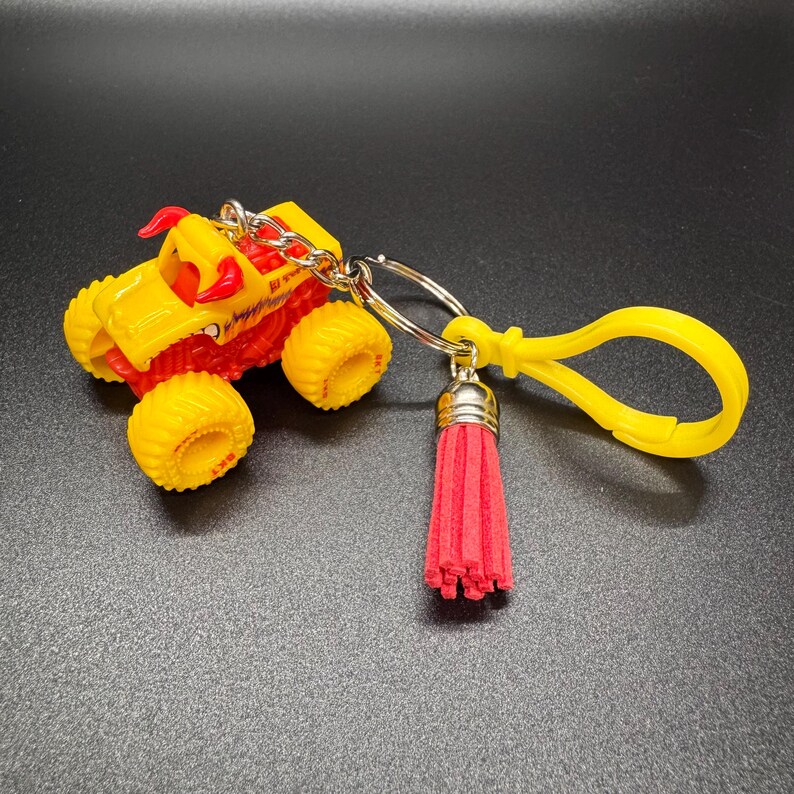 Puede incluir: Un llavero de cami&oacute;n monstruo amarillo y rojo con una borla roja y un clip amarillo. El cami&oacute;n de juguete tiene ruedas amarillas grandes y un dise&ntilde;o detallado. El llavero est&aacute; sujeto a un anillo de metal plateado.