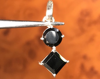 以下が含まれることがあります： 2つの黒い宝石が付いたシルバーペンダント。上の宝石は丸く、下の宝石は正方形です。