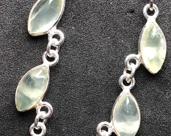 Puede incluir: Pendientes colgantes plateados con tres piedras preciosas ovaladas de color verde pálido. Las piedras están conectadas por pequeños eslabones plateados, creando un efecto en cascada. Los pendientes tienen un cierre de gancho sencillo.