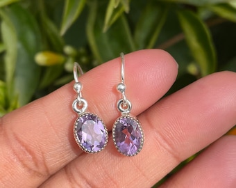 May include: A pair of silver earrings with oval-shaped amethyst gemstones. The earrings have a simple design and are perfect for everyday wear.