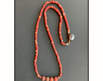 May include: A red and orange beaded necklace with a silver clasp and a larger red bead at the center.