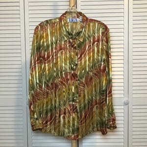 May include: A long-sleeve button-down shirt featuring a metallic finish with vertical stripes and an abstract swirling pattern in shades of gold, olive green, and deep red. The shirt has a collar and a label reading BFA at the neck.