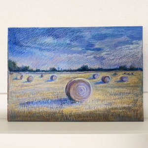 Könnte beinhalten: Eine Pastellzeichnung eines Feldes mit Heuballen. Der Himmel ist blau mit weißen Wolken. Die Heuballen sind lila und braun.