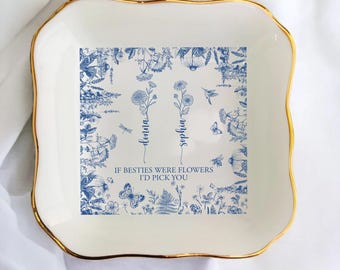 Puede incluir: Un plato de cerámica blanco con borde dorado y diseño floral azul. El plato presenta los nombres "Donna" y "Sophia" con el texto "If besties were flowers I'd pick you."