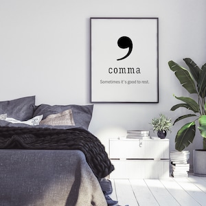 Pode incluir: Impressão tipográfica em preto e branco com uma vírgula de pontuação e o texto "comma" e "Sometimes it's good to rest." A impressão está emoldurada e pendurada em uma parede branca acima de uma mesa de cabeceira branca.