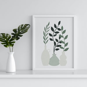Könnte beinhalten: Ein weiß gerahmter Kunstdruck mit drei Vasen mit grünen und schwarzen Blättern. Links befindet sich eine weiße Vase mit grünen Blättern. Das Kunstwerk wird auf einem weißen Regal ausgestellt.