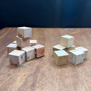 May include: A group of small, wooden blocks in various arrangements. Some blocks are stacked in a tower, while others are scattered on a wooden surface.
