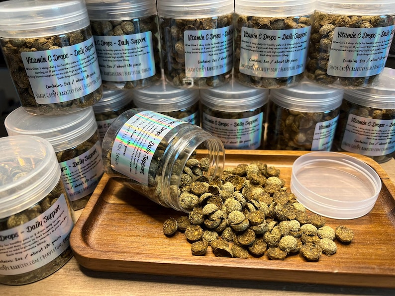 May include: A close-up of a jar filled with small, green, round vitamin C drops. The jar has a label that reads "Vitamin C Drops - Daily Support". The drops are scattered on a wooden surface.