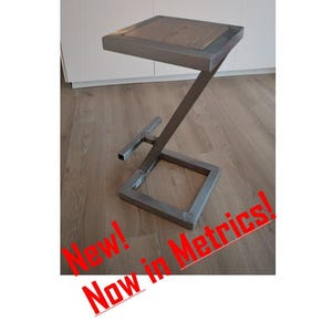 Könnte beinhalten: Ein Barhocker aus Metall und Holz mit einem Z-förmigen Fuß. Die Sitzfläche ist aus Holz und der Fuß aus Metall. Der Hocker ist in Silber lackiert. "Neu! Jetzt in metrischen Maßen!" steht in Rot auf dem Boden.