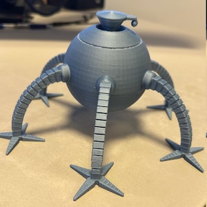 May include: A gray, 3D-printed model of a spherical robot with four articulated legs and a top-mounted cup-like structure. The legs have star-shaped feet. The robot is designed with a detailed, textured surface.