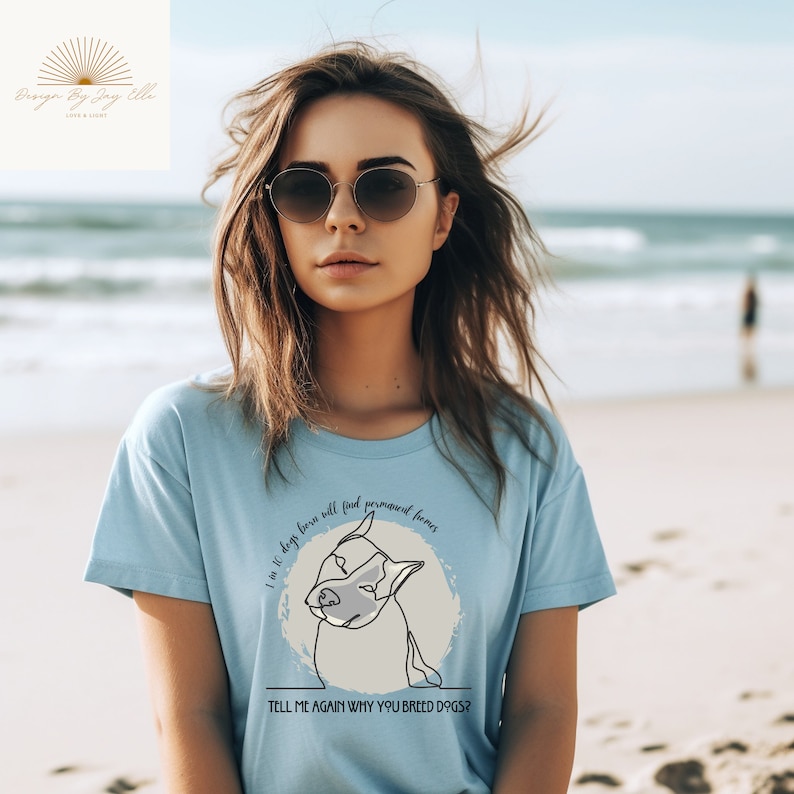 May include: Light blue t-shirt with a dog graphic and the text "I 10 dogs born will find permanent homes. TELL ME AGAIN WHY YOU BREED DOGS?". The shirt features a round neck and short sleeves.