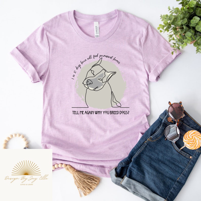 May include: A light purple t-shirt with the text "I in 10 dogs born will find permanent homes. TELL ME AGAIN WHY YOU BREED DOGS?" and a line drawing of a dog. The shirt is paired with denim shorts and sunglasses.