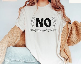 May include: Cream-colored t-shirt with the word "NO" in bold black letters, accompanied by the phrase "That's a complete sentence." Floral sprigs flank the word "NO". The shirt is made of soft material and is part of the Bella+Canvas collection.