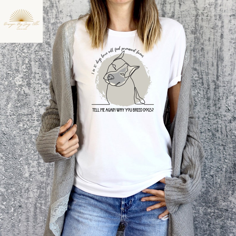 May include: White t-shirt with a line drawing of a dog inside a gray circle. The text reads, "1 in 10 dogs born will find permanent homes. Tell me again why you breed dogs?" The shirt is paired with blue jeans.
