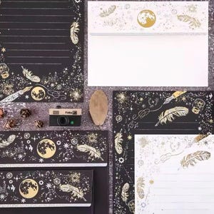 Puede incluir: Juego de papeler&iacute;a con dise&ntilde;o celestial. Fondo negro con detalles dorados de plumas, lunas y estrellas. Incluye sobres, papel de carta y una peque&ntilde;a c&aacute;mara.