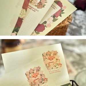 Pu&ograve; includere: Un set di quattro biglietti da lettera con sfondo verde chiaro e motivo a griglia. Ogni biglietto presenta un'illustrazione diversa di un coniglio o un cane circondato da fiori. Il testo sui biglietti recita "Life is warm days are always gentle and shining".