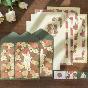 Pu&ograve; includere: Un set di cancelleria con un design floreale con coniglietti. Il set include buste, carta da lettere e un foglio di adesivi. Le buste e la carta da lettere hanno un bordo verde con un motivo floreale e un coniglietto bianco al centro. Il foglio di adesivi ha un motivo floreale con un coniglietto bianco al centro.