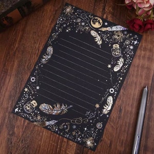 Puede incluir: Papel de papeler&iacute;a negro con detalles dorados. El papel presenta un borde de estrellas, plumas y dise&ntilde;os celestiales. Rayado para escribir, incluye un bol&iacute;grafo y es adecuado para cartas o notas.