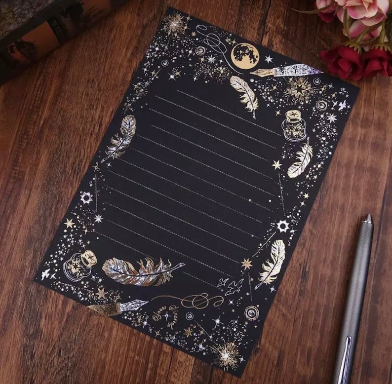 Puede incluir: Papel de papeler&iacute;a negro con detalles dorados. El papel presenta un borde de estrellas, plumas y dise&ntilde;os celestiales. Rayado para escribir, incluye un bol&iacute;grafo y es adecuado para cartas o notas.