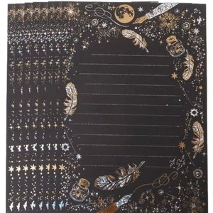 Puede incluir: Un mont&oacute;n de hojas de papeler&iacute;a negras con un dise&ntilde;o celestial. Las hojas presentan detalles dorados y plateados de estrellas, plumas y tinteros. Las p&aacute;ginas rayadas est&aacute;n rodeadas de elementos decorativos.