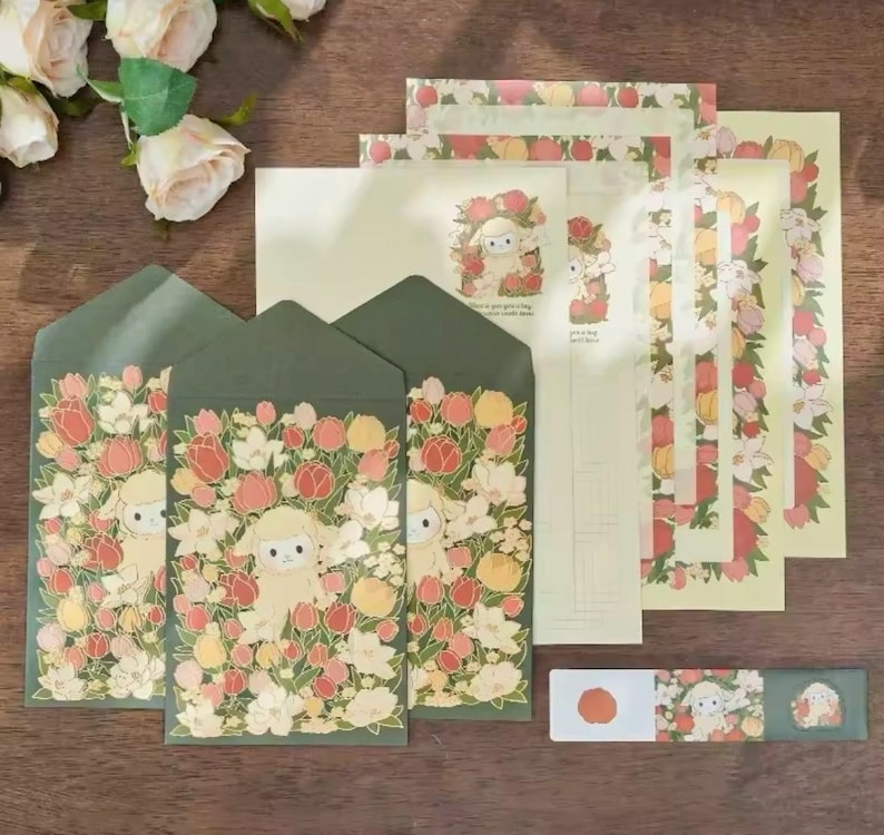 Pu&ograve; includere: Un set di cancelleria con un design floreale con un agnello al centro. Il set include buste, carta da lettere e un foglio di adesivi. Le buste sono verdi con un motivo floreale e un agnello al centro. La carta da lettere &egrave; crema con un bordo floreale e un agnello al centro. Il foglio di adesivi ha un design floreale con un agnello al centro.