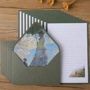 Pu&ograve; includere: Un set di cartoleria verde con carta bianca rigata e buste. Le buste hanno una finestra che mostra un dipinto di una donna con un ombrello.